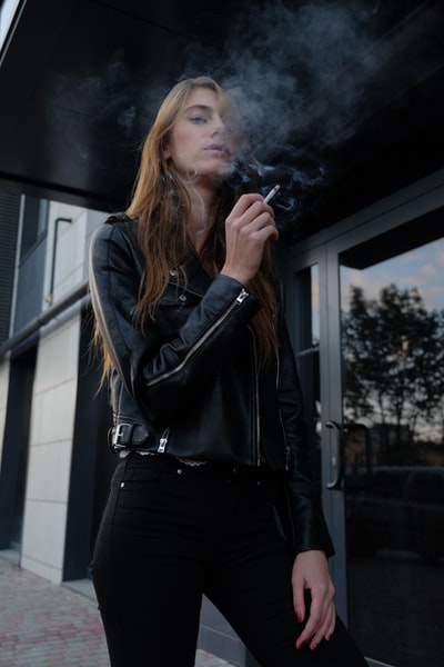 穿着黑色皮夹克的女人在街上抽烟